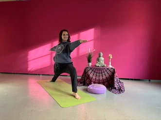 Yoga im Museum mit Katja Lüdenbach Eine Frau macht Yoga im Krieger II Pose auf einer Matte vor einer pinken Wand im Studio.