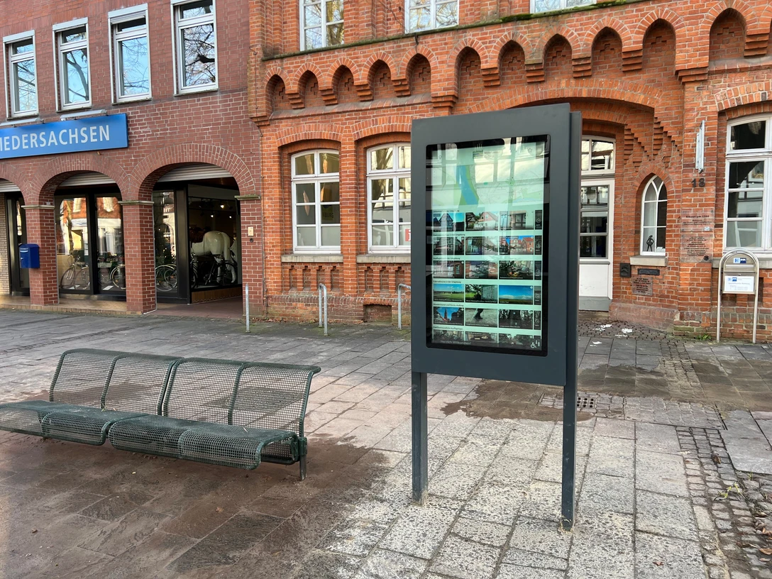 Infoterminal Ein digitaler Infoterminal in städtischer Umgebung vor Backsteingebäude und Sitzbank.