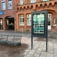 Infoterminal Ein digitaler Infoterminal in städtischer Umgebung vor Backsteingebäude und Sitzbank.
