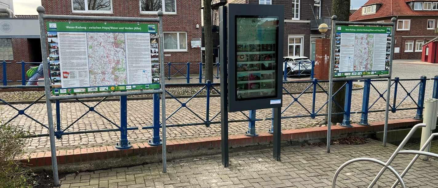 A modern outdoor information kiosk provides digital information against the backdrop of traditional brick architecture.