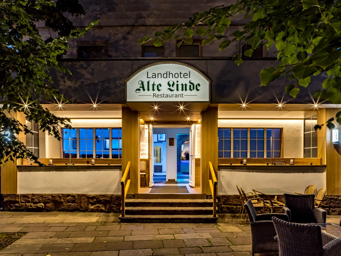 Eingang vom Landhotel Alte Linde Würgassen Beleuchteter Eingang mit drei Treppenstufen und Geländer, seitlich rechts Terrassenbestuhlung