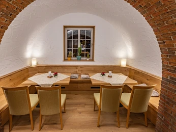 Saal vom Landhotel Alte Linde Würgassen Ecknische mit Rundbogen des Saales, zwei Holztische mit jeweils zwei Stühlen durchgehende Sitzbank aus Holz, im Hintergrund ein Fenster