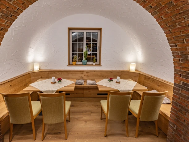 Saal vom Landhotel Alte Linde Würgassen Ecknische mit Rundbogen des Saales, zwei Holztische mit jeweils zwei Stühlen durchgehende Sitzbank aus Holz, im Hintergrund ein Fenster