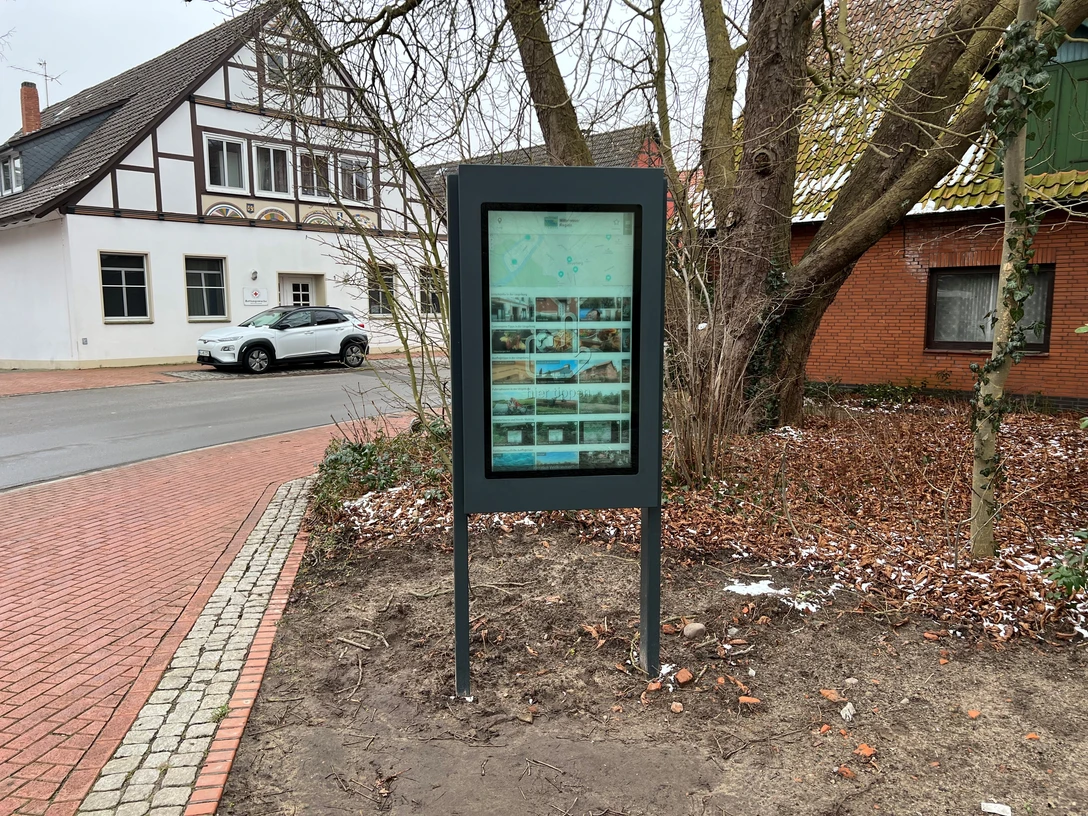 Infoterminal Steyerberg Infoterminal Steyerberg zeigt einen digitalen Bildschirm vor einem Fachwerkgebäude an einer Straßenecke an.