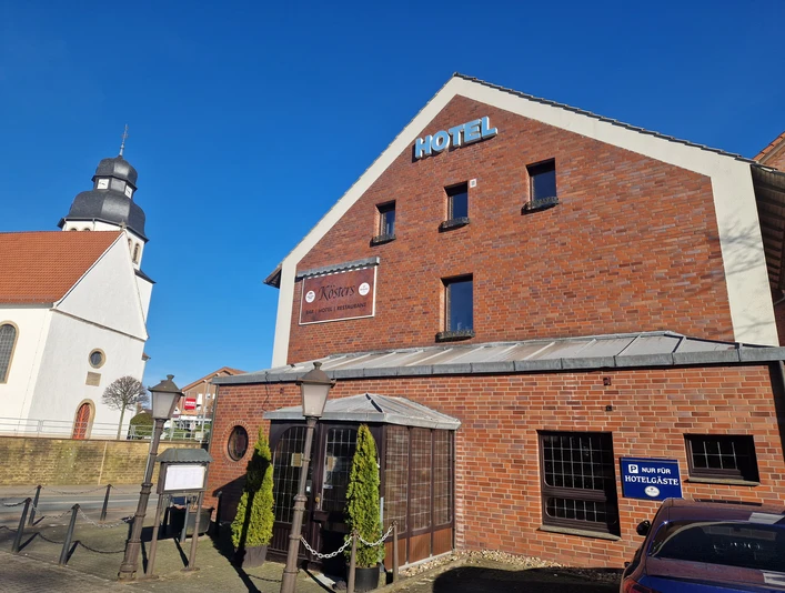 Hotel Kösters in Backsteinoptik, rechts ein Parkplatzschild, links die Kirche mit Zwiebelturm.