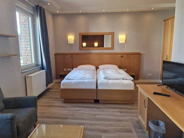 Zwei Einzelbetten in einem modern eingerichteten Hotelzimmer, mit Sessel, Tisch und Flachbildfernseher.