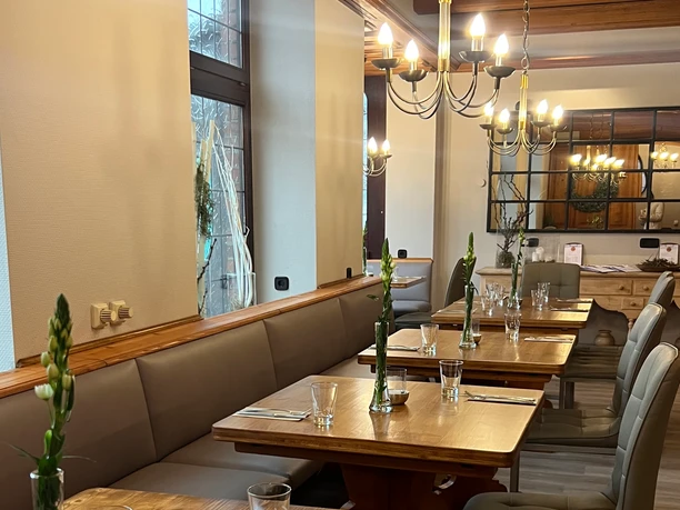 Elegantes Restaurant mit Holztischen und bequemen Sitzbänken, dezent dekoriert mit frischen Blumen.