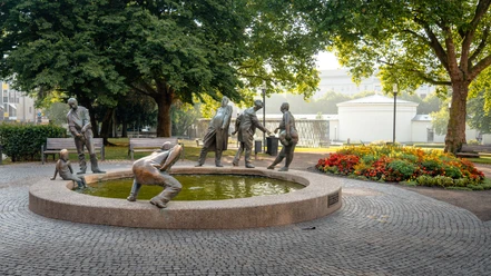 Die Skulptur „Kreislauf des Geldes“ zeigt sechs bronzene Figuren, die Geiz, Gier, Gönnerhaftigkeit und Bettelei symbolisieren. Er befindet sich vor einem Park.