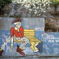 Street Art Führung-Aachener Innenstadt Zwischen den Tagen (c) Regina Weinkauf.jpg Graffiti einer Punk-Person auf einer Bank mit der Aufschrift „Zwischen den Tagen“ vor einer alten Mauer.