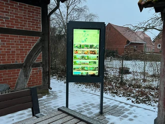 A modern information kiosk with a backlit display in an outdoor setting, surrounded by snow-covered structures.
