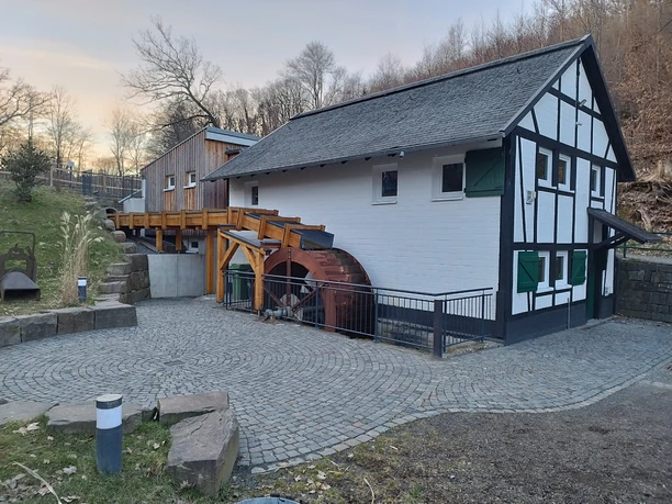 Dümmlinghauser Mühle Traditionelle Wassermühle mit hölzernem Wasserrad und Fachwerk, umgeben von Bäumen und Kopfsteinpflaster.
