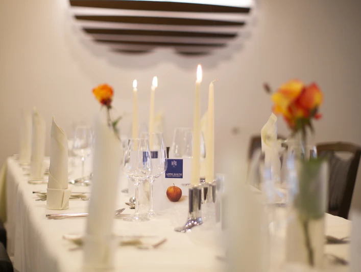 Gedeckter Tisch im Gütsel Ein festlich gedeckter Tisch mit weißen Tischtüchern, Kerzen und orangen Rosen in einem eleganten Raum.