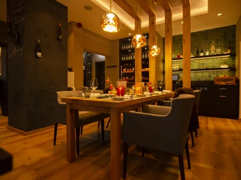 Das Restaurant für besondere Momente Gemütliches Restaurant mit Holzelementen, gedimmtem Licht und stilvoll gedecktem Tisch für vier Personen.