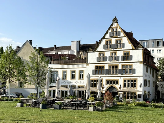 Galerie Hotel.JPEG Hotel mit weißer Fassade und hölzernen Fensterläden, Terrasse mit Tischen und Stühlen im Vordergrund.