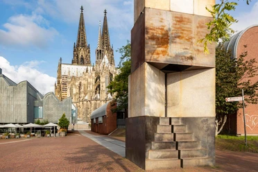 MAALOT Skulptur „MA'ALOT“ von Dani Karavan vor dem Kölner Dom bei sonnigem Himmel.