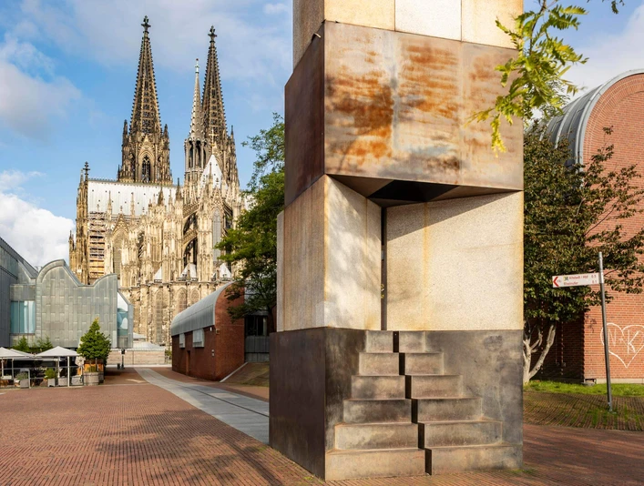MAALOT Skulptur „MA'ALOT“ von Dani Karavan vor dem Kölner Dom bei sonnigem Himmel.Sculpture "MA'ALOT" by Dani Karavan in front of Cologne Cathedral under a sunny sky.