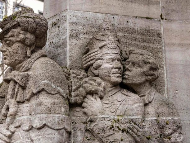 Ostermann-Brunnen Steinrelief des Ostermann-Brunnens in Köln: Drei Figuren in detailreicher Darstellung.