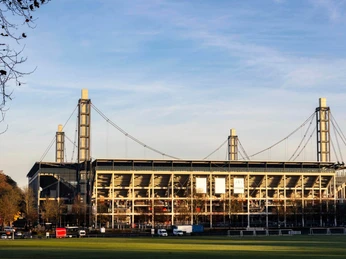 RheinEnergieSTADION RheinEnergieSTADION in Köln, umgeben von Bäumen und grüner Rasenfläche.RheinEnergieSTADION in Cologne, surrounded by trees and green lawns.