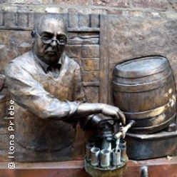 Bronzerelief eines Mannes beim Zapfen aus einem Fass mit mehreren Gläsern.