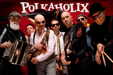 Musiker der Band Polkaholix in stilvollen Outfits mit Instrumenten wie Saxophon und Trompete.