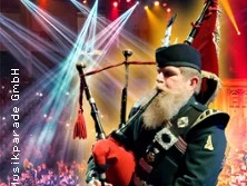 Ein Dudelsackspieler in traditioneller schottischer Tracht vor einer Bühne mit bunten Lichteffekten.