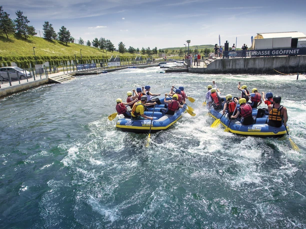 Leipzig Region_Kanupark Markleeberg©Katja Fouad Vollmer (20).jpg Kanutouristen paddeln auf sprudelndem Wasser in einem Freizeitpark bei sonnigem Wetter.