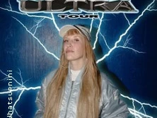 Ein Mann mit Baseballkappe, langen Haaren und glänzender Jacke steht vor einer Blitzhintergrundkulisse.