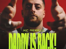 KC Rebell posiert frontal vor einem roten Hintergrund, lässig mit ausgestreckten Armen.