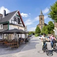 In Wülfrath-Düssel unterwegs Zwei Menschen fahren auf Fahrrädern eine Straße entlang, vorbei an Fachwerkhäusern und einer Kirche in Wülfrath-Düssel.