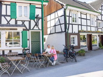 Einkehr in den Kutscherstuben in Wülfrath-Düssel Zwei Menschen sitzen bei Sonnenschein an einem Tisch vor einem Fachwerkhaus mit grünen Fensterläden.
