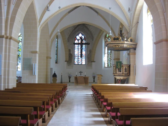 Bild 001.jpg Innenansicht einer Kirche mit hellem, gotischem Gewölbe, Holzbänken und bunten Glasfenstern.