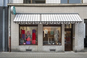 rock-it-baby Das Bild zeigt eine Ladenfassade in stilvollem Mosaikdesign. Vor den Schaufenstern hängt eine gestreifte Markise.