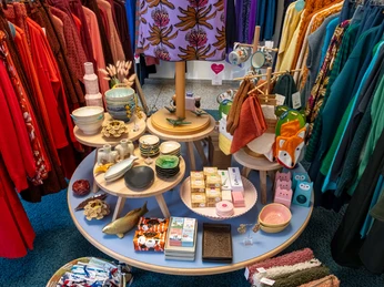 rock-it-baby Ein rundes Regal zeigt bunte Kleidung, Keramikschalen, Tücher und Dekoration in lebhaften Farben.A round shelf displays colorful clothes, ceramic bowls, scarves and decorations in vibrant colors.