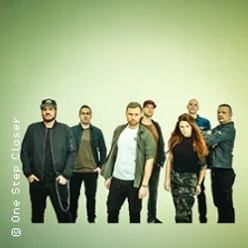 Eine siebenköpfige Band steht vor einem hellen Hintergrund.