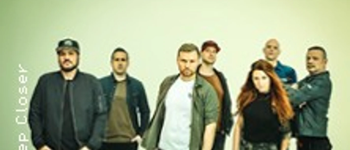 Eine siebenköpfige Band steht vor einem hellen Hintergrund.