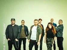 Eine siebenköpfige Band steht vor einem hellen Hintergrund.