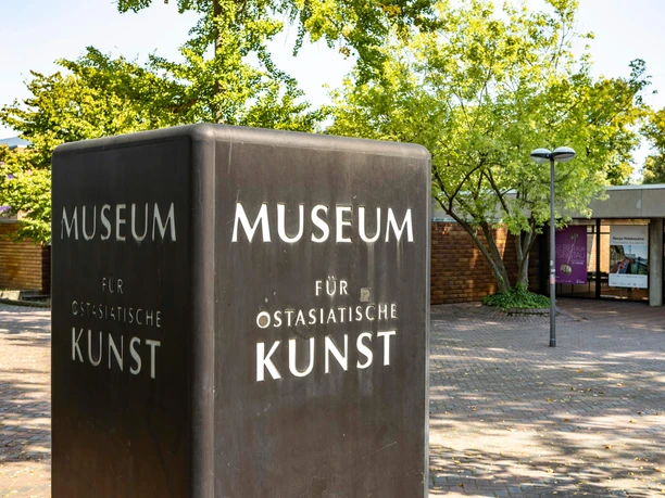 Museum für Ostasiatische Kunst Museum für Ostasiatische Kunst in Köln, moderner Bau mit dunklem Schild, grüne Bäume im Hintergrund.
