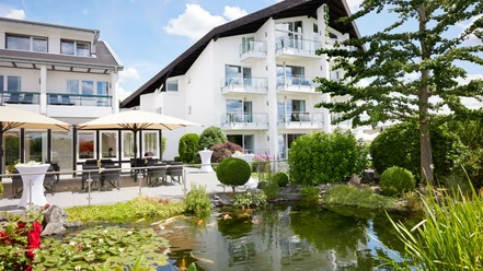 Außenansicht Modernes Hotel mit weißen Balkonen, umgeben von grüner Gartenanlage und Teich mit Seerosen.