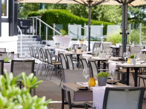Derichsweiler Hof Elegante Außenbestuhlung eines Restaurants, sonnendurchflutet, mit gedeckten Tischen und Pflanzen.