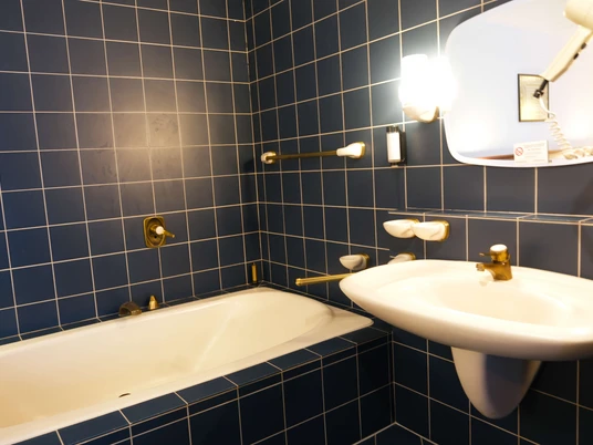 Badezimmer im Deluxe-Zimmer im Stargaze Home Hotel in Haan Badewanne mit blauen Fliesen, Waschbecken und Spiegel mit Wandbeleuchtung im Hotelzimmer.