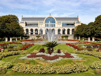 Flora and botanical garden Das Bild zeigt die imposante historische Fassade der Flora in Köln, umrundet von blühenden Gärten und einem zentralen Springbrunnen. Der gepflegte Park und die symmetrisch angelegten Blumenbeete verleihen dem Ort eine malerische Eleganz, während die Architektur des Gebäudes durch ihre Bögen und Fenster beeindruckt.The picture shows the imposing historic façade of the Flora in Cologne, surrounded by flowering gardens and a central fountain. The well-tended park and the symmetrically arranged flowerbeds lend the place a picturesque elegance, while the architecture of the building impresses with its arches and windows.