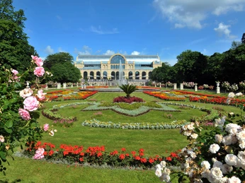 Flora und Botanischer Garten Im Bild ist die historische Flora in Köln zu sehen, umgeben von prächtig blühenden Gartenanlagen, deren symmetrisch angelegte Blumenbeete eine farbenfrohe Vielfalt zeigen. Im Vordergrund zieren Rosen die Szenerie, während im Hintergrund das denkmalgeschützte Gebäude majestätisch in den Himmel ragt. The picture shows the historic Flora in Cologne, surrounded by magnificently blooming gardens, whose symmetrically arranged flowerbeds display a colorful variety. Roses adorn the scenery in the foreground, while the listed building rises majestically into the sky in the background.