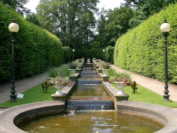 Flora und Botanischer Garten Kaskadenbrunnen umrahmt von üppigem Laub, Pflanzenkübeln und Laternen, lädt zum Entspannen ein.