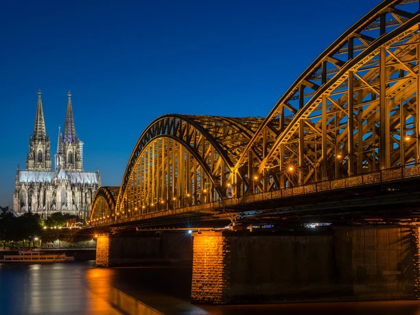 Hohenzollern Bridge Cologne Cathedral, illuminated at night, rises majestically next to the Hohenzollern Bridge, which crosses the Rhine.