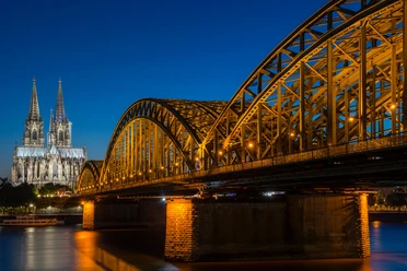 Hohenzollernbrücke Der Kölner Dom, erleuchtet in der Nacht, erhebt sich majestätisch neben der Hohenzollernbrücke, die über den Rhein führt.