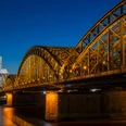 Hohenzollernbrücke Der Kölner Dom, erleuchtet in der Nacht, erhebt sich majestätisch neben der Hohenzollernbrücke, die über den Rhein führt.Cologne Cathedral, illuminated at night, rises majestically next to the Hohenzollern Bridge, which crosses the Rhine.