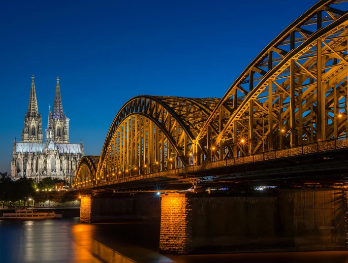 Hohenzollernbrücke Der Kölner Dom, erleuchtet in der Nacht, erhebt sich majestätisch neben der Hohenzollernbrücke, die über den Rhein führt.Cologne Cathedral, illuminated at night, rises majestically next to the Hohenzollern Bridge, which crosses the Rhine.