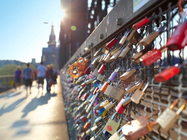 Hohenzollern Bridge The picture shows numerous colorful love locks hanging closely on a metal lattice, with Cologne Cathedral in the background in the sunshine.
