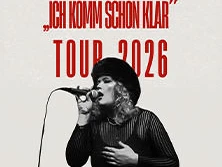 Sängerin mit schwarzem Hut und Mikrofon performt auf Bühne. Hintergrund mit Tourdaten für 2026.