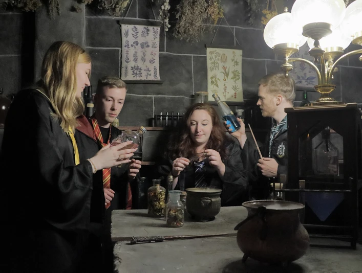 Escape-Room Bad Oeynhausen Vier Personen in Fantasiekostümen experimentieren in einem mystischen Kräuterlabor mit Utensilien.
